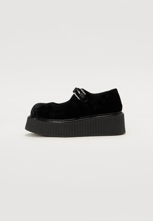 Sapatos de plataforma pretos com acabamento em veludo mate, bico arredondado, tira com fivela e sola texturizada e estriada.
