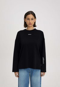 Czarny longsleeve z okrągłym dekoltem i luźnym krojem. Posiada biały napis "MISAGA" na piersi oraz "adklisure" na rękawie.