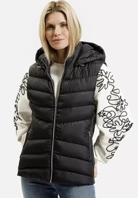 Kamizelka puchowa w czarnym kolorze, z kapturem i zapięciem na zamek. Rękawy w białym kolorze z czarnymi abstrakcyjnymi haftami. Miękka, pikowana struktura.