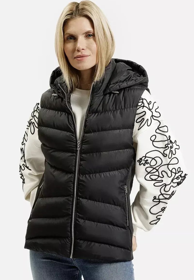 Kamizelka puchowa w czarnym kolorze, z kapturem i zapięciem na zamek. Rękawy w białym kolorze z czarnymi abstrakcyjnymi haftami. Miękka, pikowana struktura.