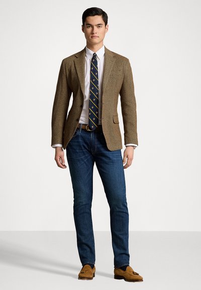 Bruin visgraatblazer, wit shirt, marineblauwe stropdas met gele accenten, blauwe spijkerbroek en tan loafers. Eenvoudige, op maat gemaakte pasvorm met zakken.
