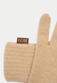Gant en laine beige tricoté avec un poignet côtelé et une étiquette de marque GOBI marron sur fond blanc.