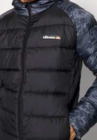 Svart puffjacka med dragkedja, med ett mönstrat mörkblått axeldesign och en ellesse-logotyp på bröstet.