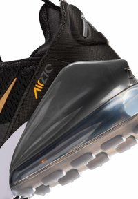 Μαύρη και γκρι φτέρνα αθλητικού παπουτσιού με διάφανο αερόσολα, πορτοκαλί κείμενο "Air 270" και χρυσό λογότυπο swoosh σε ύφασμα από δίχτυ.