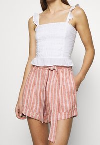 Witte ruffeltop met geschurde textuur, gecombineerd met koraalkleurige gestreepte shorts met een strikceintuur en zijzakken.