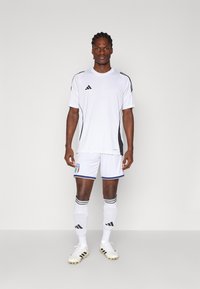 White short-sleeve jersey with black stripes, paired with white shorts featuring a blue trim and Italian flag. White socks and cleats complete the look.