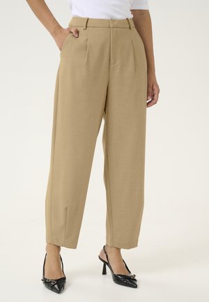 Beige maßgeschneiderte Hosen mit hohem Taillendesign, Falten, seitlichen Taschen und lockerer Passform. Kombiniert mit spitzen schwarzen High-Heels.