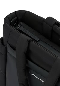 Mochila negra acolchada con parte superior con cremallera, que presenta un tejido suave, asas resistentes y una etiqueta con el logotipo. Diseño elegante y minimalista.