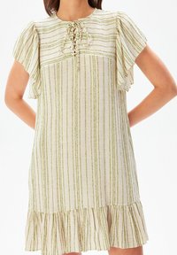 Vaalean värinen mekko, jossa on pystysuoria vihreitä raitoja, lyhyet röyhelöhihaiset hihat, nauhakuptuksen kaula-aukko ja röyhelöhelma alareunassa.