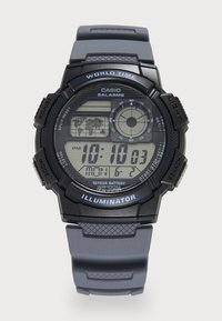 Montre numérique Casio au design noir et gris, avec un bracelet en caoutchouc, un cadran rond, un écran LCD et des accents bleus. Les fonctionnalités incluent une alarme et un rétroéclairage.