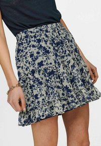 Květinová sukně s námořnickomodrým a světle šedým vzorem, volánkovým lemem a elastickým pasem. Vyrobena z lehké, texturované tkaniny.