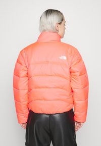 Giacca a vento fucsia con colletto alto, sezioni trapuntate e logo ricamato sul retro. Il materiale sembra lucido e imbottito.
