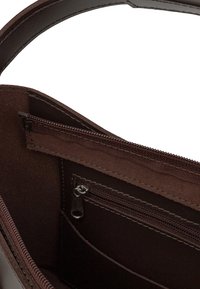Mörkbrun läderväska med inredning som visar ett litet blixtlåsfack, sydda sömmar och en del av handtaget.
