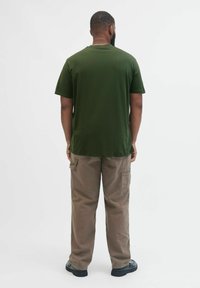 Dunkelgrünes Baumwoll-T-Shirt mit kurzen Ärmeln und schlichter Gestaltung, kombiniert mit hellbraunen Cargo-Hosen mit Seitentaschen.