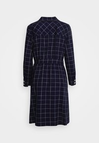 Marinblå rutigt klänning med långa ärmar, en figurnära midja, knapppdetaljer på ärmsluten och en bakre yoke. Tyget har ett rutmönster i blått.