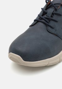 Chaussure synthétique bleue avec une texture lisse, dotée de lacets sombres, d'une semelle en caoutchouc beige et d'un design de pointe arrondie.