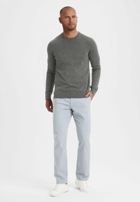 Grauer Langarmpullover, leichtes Strickmaterial; kombiniert mit hellblauen Hosen; weiße Sneakers runden das Outfit ab.