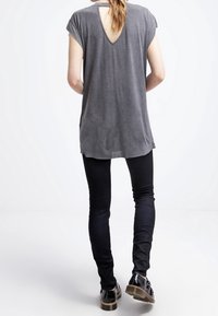 Grå kortärmad topp med V-ringning och skärning i ryggen, kombinerad med åtsittande svarta byxor och svarta skor med tjock sula.