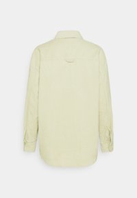 Chemise en velours côtelé jaune clair à manches longues vue de dos avec un col classique et des poignets boutonnés.