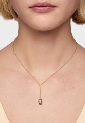 Delicado collar de cadena de oro con un colgante vertical que presenta un centro rectangular de oro enmarcado por pequeñas piedras negras en el cuello de una mujer.