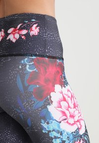 Kukkakuvioiset leggingsit, joissa on tumma tausta ja kirkkaan vaaleanpunaisia ja sinisiä kukka-kuvioita. Ne on valmistettu joustavasta kankaasta, jossa on korkea vyötärö ja teksturoitu muotoilu.