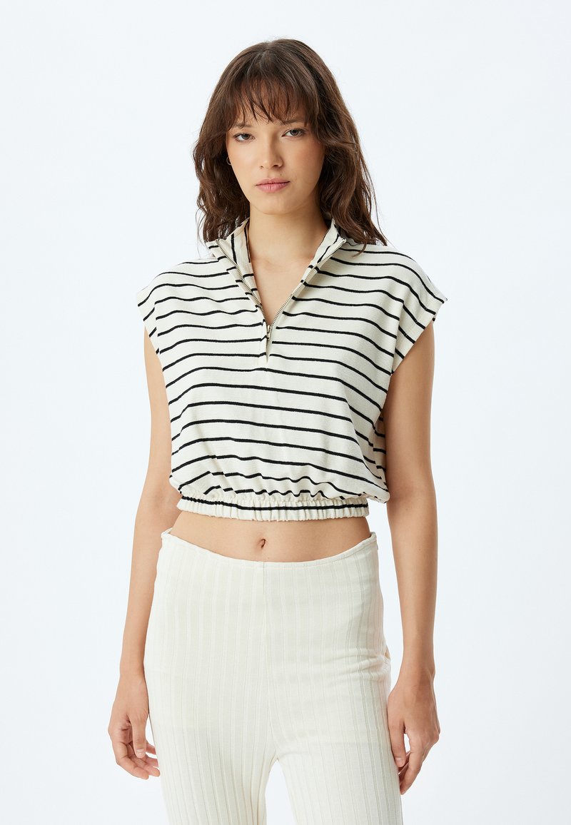 Gestreepte crop top in crème en zwart, met een hoge halslijn met een rits, korte mouwen en een elastische zoom. Gecombineerd met geribbelde crème broek.