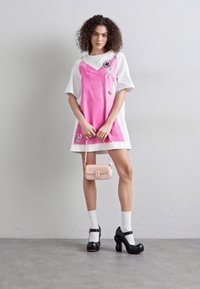 Rosa en witte jurk met korte mouwen, zwarte hoge hakken, witte sokken en een kleine roze handtas. Bevat patches op de jurk.