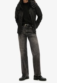 Svart vadderad jacka med dragkedja, kombinerad med urtvättade svarta raka jeans och svarta snörkängor. Strukturerad tyg med en avslappnad passform.