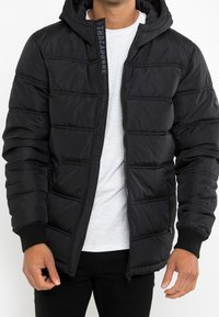 Czarna kurtka puchowa z kapturem, z poziomym przeszyciem, zapięciem na zamek, ściągaczami przy rękawach oraz detalem logo wzdłuż zamka.