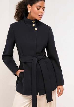 Navy blue coat with a high collar, belted waist, and gold button accents. Made from textured fabric, featuring two side pockets.