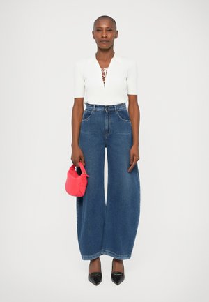 Haut blanc à manches courtes côtelé avec des détails en dentelle, jean en denim bleu à taille haute et jambes larges, et un petit sac à main rose. Escarpins noirs à bout pointu.