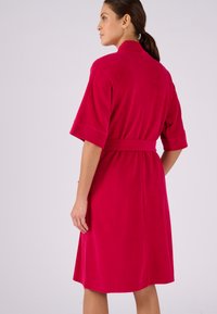 Fuchsia badjas met een gestructureerde afwerking, voorzien van een ceintuur op de taille en korte, brede mouwen. Het ontwerp is knielang met een rechte silhoutte.