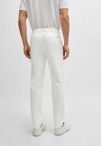 Vita byxor med slim fit, slät textur och två bakfickor. I kombination med ljusa sneakers, sedd bakifrån.