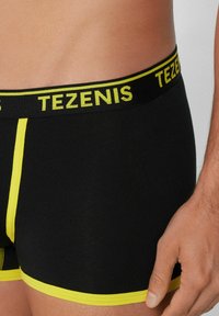 Boxer shorts negros con cinturilla de logo amarillo y costuras amarillas. Presentan un ajuste ceñido y una textura suave.