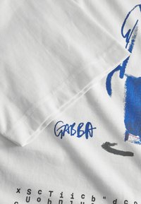 Tricou alb din bumbac, cu un design grafic abstract în nuanțe de albastru și negru, cu text imprimat și un tiv vizibil cusut.