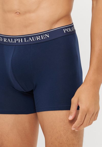 Boxers de cor azul-marinho com uma faixa contrastante onde se lê "POLO RALPH LAUREN". O material é suave com um design ajustado.