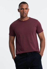 Bordeaux-farbenes T-Shirt mit kurzen Ärmeln aus weichem Stoff und Rundhalsausschnitt, kombiniert mit dunklen Hosen. Der Schnitt ist lässig und entspannt.