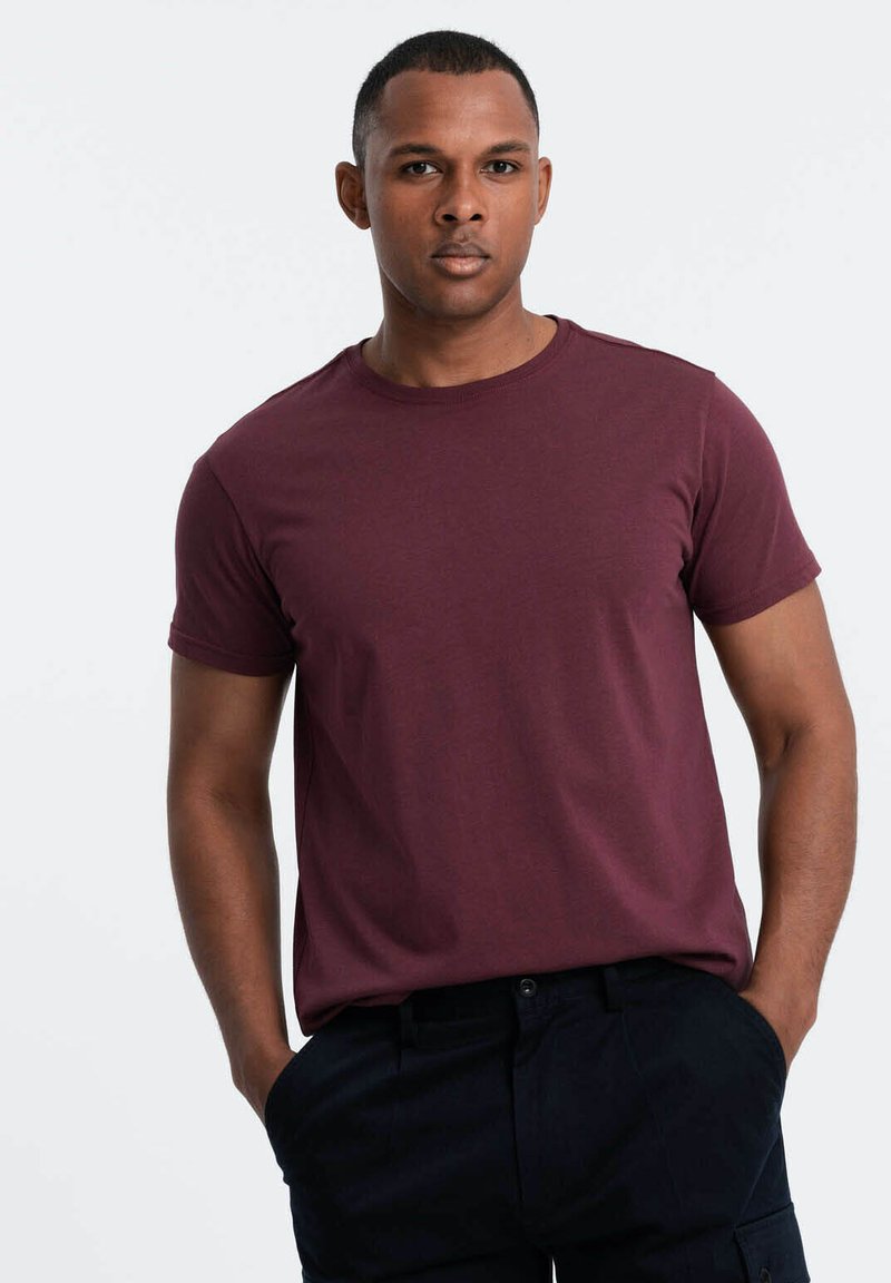 Bordeaux-farbenes T-Shirt mit kurzen Ärmeln aus weichem Stoff und Rundhalsausschnitt, kombiniert mit dunklen Hosen. Der Schnitt ist lässig und entspannt.