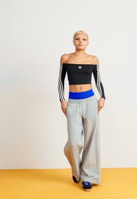 Μαύρο cropped τοπ με σχέδιο χωρίς ώμους; μπλε ελαστική ζώνη με γκρι φαρδιά φόρμες; μοντέλο που φορά μαύρα αθλητικά παπούτσια.