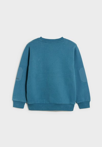 Felpa blu con maniche lunghe, colletto e polsini a coste, tessuto strutturato e una toppa a contrasto sulla manica sinistra.