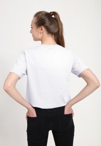 Bílé bavlněné tričko s krátkými rukávy a klasickým kulatým výstřihem, nošené s těsnými černými džíny, představující jednoduchý a čistý design.