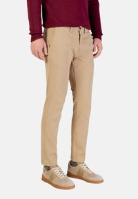 Chinos beiges à coupe slim, dotés d'une braguette zippée et de poches latérales, associés à des baskets gris clair et marron clair. Portés avec un pull bordeaux.