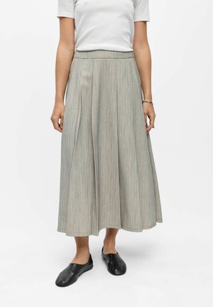 Femme portant un haut blanc à manches courtes, une jupe midi plissée gris clair, des chaussures noires sans lacets et un bracelet à son poignet droit.