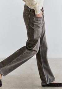 Gray denim jeans with a relaxed fit, featuring side pockets, subtle whiskering, and clean, straight seams. Worn with black flats.