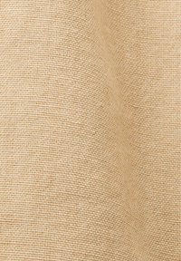 Tissu beige tissé avec un motif texturé et de légers plis créant de douces ombres et de la profondeur.