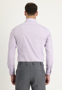 Camicia viola chiaro con maniche lunghe e polsini con bottoni, abbinata a pantaloni grigi. Sono visibili i dettagli dei bottoni e la morbida trama del tessuto.