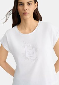 T-shirt blanc à manches courtes roulées, présentant un motif en cristaux des lettres "LJ" au centre, en coton lisse.