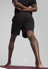 Sorte atletiske shorts lavet af letvægtsstof, med en elastisk talje og en afslappet pasform, vist på en person i en stående stilling.