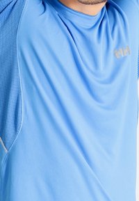 Blå idrottströja i lätt och ventilerande tyg. Har mesh-paneler, en avslappnad passform och en subtil logotyp på axeln.