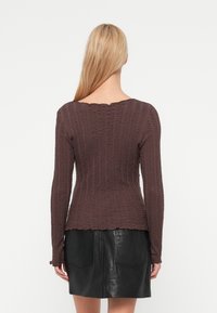 Μπλούζα με μακριά μανίκια, υφασμάτινη σε σκούρο καφέ χρώμα με σχέδιο ρυτίδων και λαιμόκοψη με κυματιστά σχέδια. Συνδυάζεται με μαύρη δερμάτινη φούστα, με δύο πίσω τσέπες.